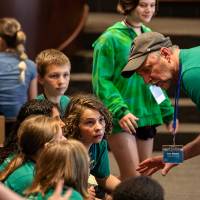 teacher in green shirt talking to students in front row of audience at awards at student project showcase